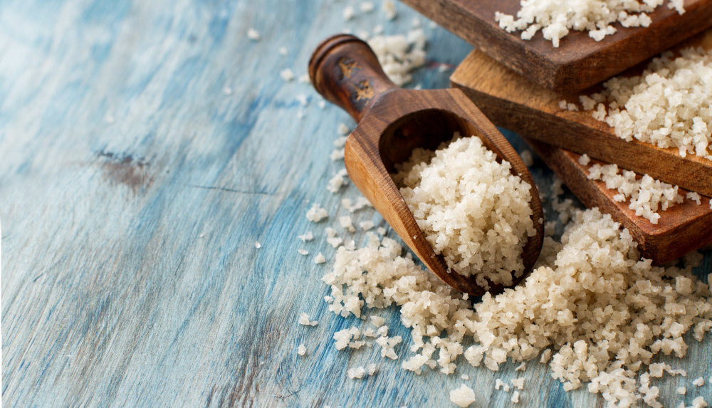 Wooden scoop filled with white granulated celtic sea salt on a blue wooden surface