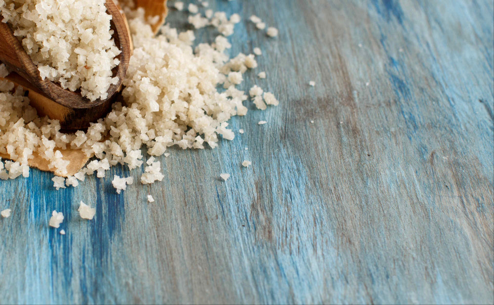 Wooden scoop filled with white granulated celtic sea salt on a blue wooden surface