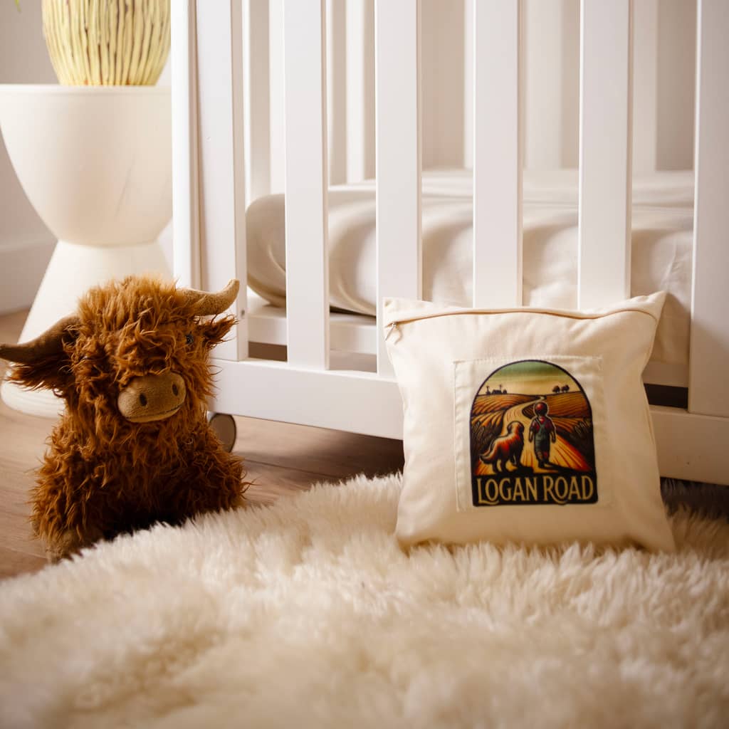 Plush toy cow and pillow with 'Logan Road' design on a soft surface.