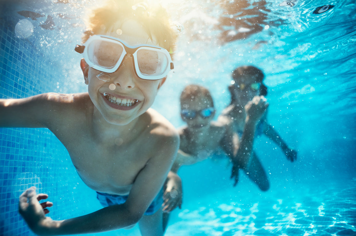 Children swimming underwater in a pool with goggles on.